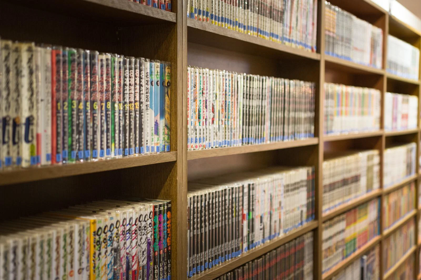 さまざまな漫画の単行本が木製の本棚に並ぶ実写の参考写真
